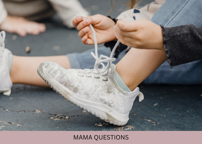 A child’s hands work on tying the laces of a white sneaker.